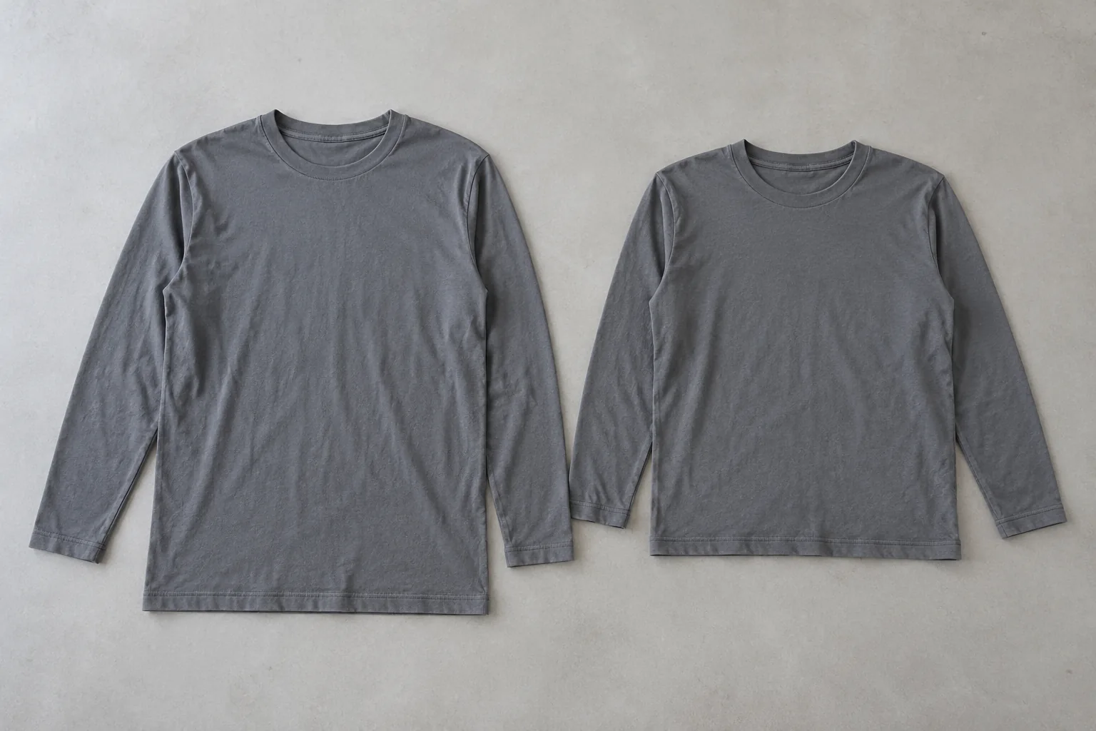 Photorealistic apparel factory documentary photograph of two finished plain slate cotton long-sleeve tees laid flat side