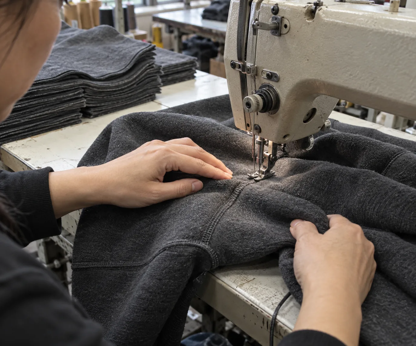 Operator sewing a heavyweight sweatshirt seam beside stacked matching panels