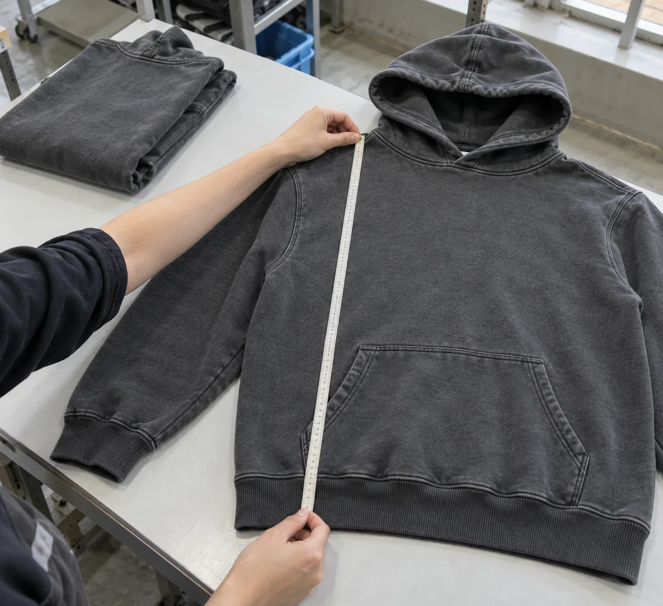 Quality technician measuring a washed hoodie laid flat on an inspection bench
