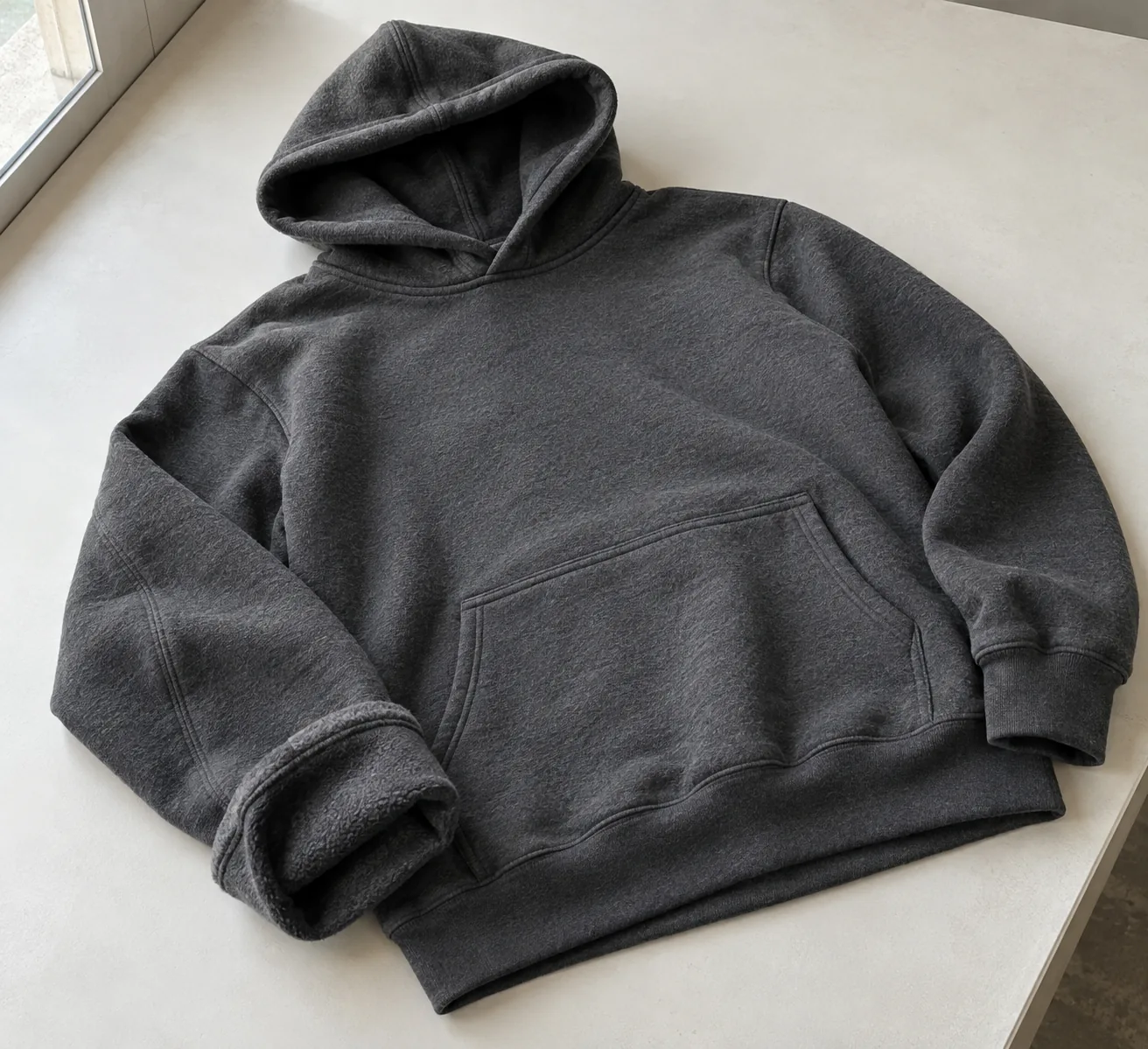 Photorealistic apparel documentary photograph of a finished unbranded charcoal fleece hoodie on a clean inspection bench
