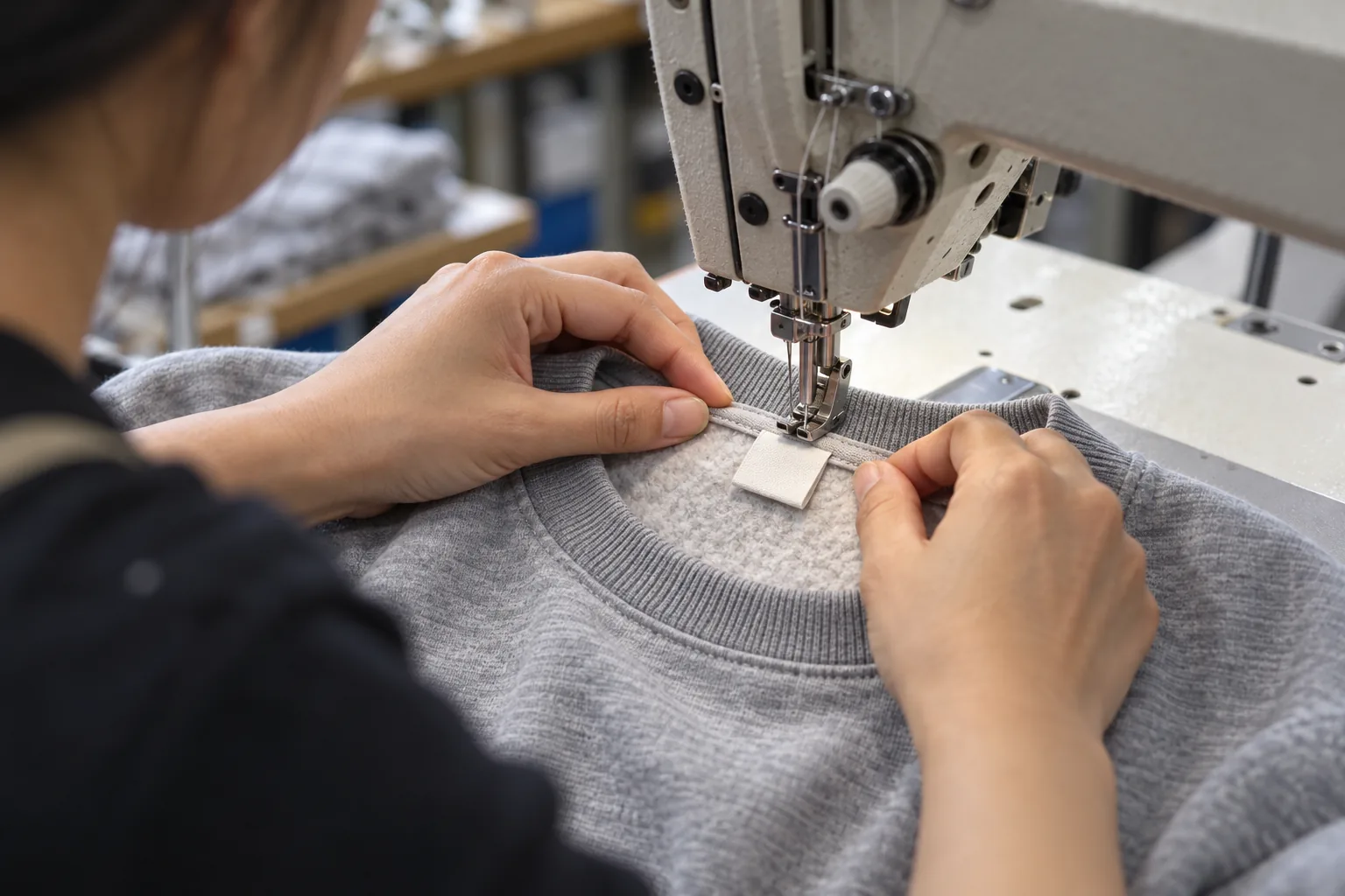 Sewing operator positioning a plain folded label inside a sweatshirt neckline
