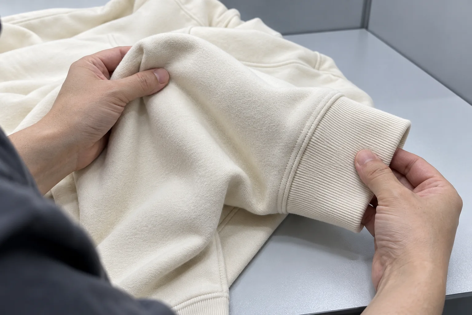 Quality inspector comparing a cream hoodie body and rib cuff under neutral inspection lighting